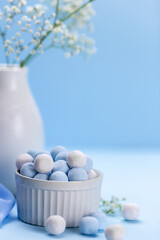 Fototapeta na wymiar White vase with flowers on a blue background. Ball candies, sweets in a vase. Place for your text.