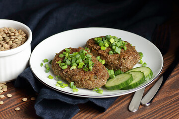 Lentil cutlets garnished with green onions and cucumber on rustic wooden table, closeup, vegetarian lenten eastern dish, healthy vegan food concept