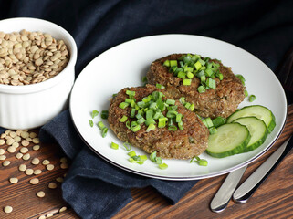 Lentil cutlets garnished with green onions and cucumber on rustic wooden table, closeup, vegetarian lenten eastern dish, healthy vegan food concept