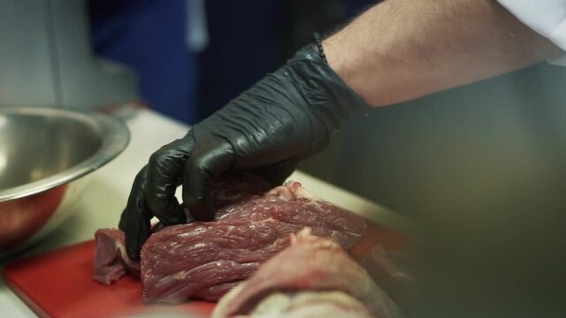 Hand of chef cuts meat with knife. Close up and slow motion