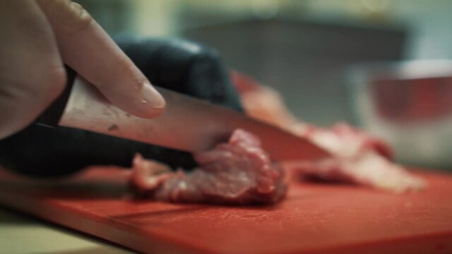 Hand of chef slices meat with knife. Close up and slow motion