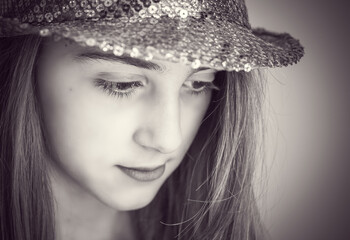 Monochrome closeup of a young girl with bright, shiny hat, looking down