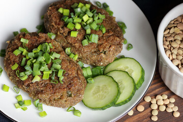 Lentil cutlets garnished with green onions and cucumber on rustic wooden table, closeup, vegetarian lenten eastern dish, healthy vegan food concept