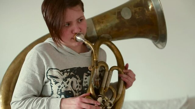 Teenager plays with lips Helicon. She blows into the mouthpiece of the trumpet, makes a low sound. Recording music for a new song.