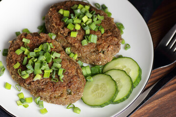 Lentil cutlets garnished with green onions and cucumber on rustic wooden table, closeup, vegetarian lenten eastern dish, healthy vegan food concept