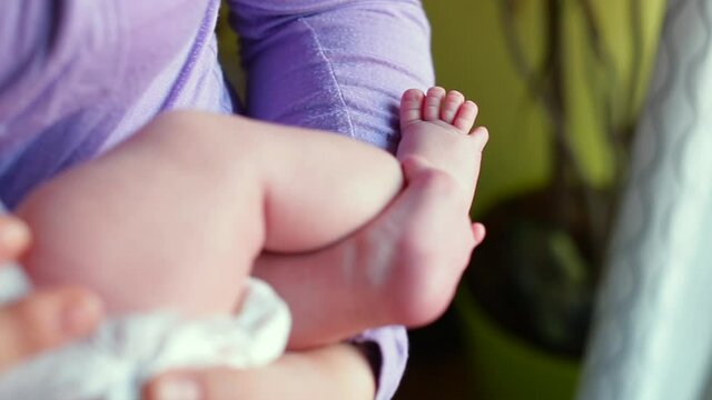 Mother's hands are holding a newborn baby. A comfortable place for a newborn, a mental connection. Camera movement to the legs. The kid moves his toes.