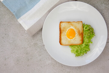 Scrambled eggs in toast on a light blue plate with with green lettuce on a gray stone background.