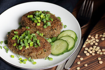 Lentil cutlets garnished with green onions and cucumber on rustic wooden table, closeup, vegetarian lenten eastern dish, healthy vegan food concept