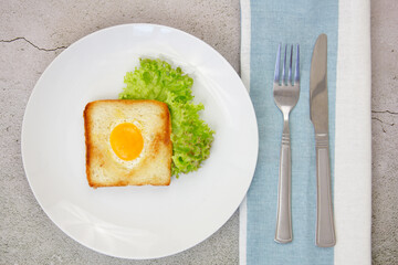Scrambled eggs in toast on a light gray plate with a green lettuce on a gray stone background with a towel and utensils. Breakfast. The concept of healthy eating.