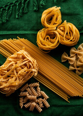 Mix of different varieties of pasta on green fabric background, cooking assorted macaroni concept