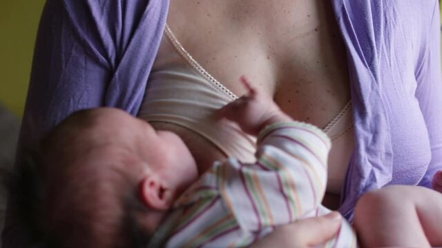 A young mother is breastfeeding her baby. He lies on his hands and moves his hands. Reflex of the newborn when eating.