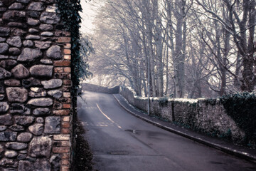 Picturesque Snowy Lane with Ancient Irish Stonework Walls and bare forest