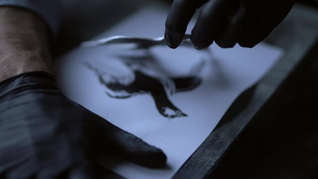 Linocut concept. Man in black gloves making lithograph stamp on paper. Handcrafting artist. 4k footage