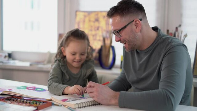 Caring caucasian dad babysitter drawing with colored pencils teaching child girl sitting at the table, father enjoy helping kid daughter playing doing homework at home, happy family creative activity