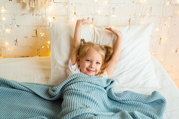 beautiful little girl lies on a bed under a blanket