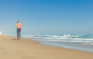 Girl running sport in the beach with covid mask and a blue sky and a blue sea with whit waves.