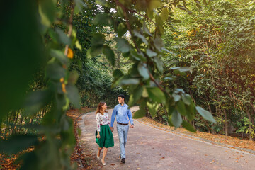 of a young loving couple walking along a path through a greenery park. A man and a woman are...