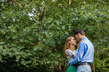 beautiful loving couple in the park look at each other hug on the background of green trees