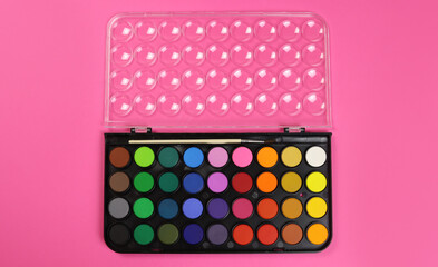 watercolour paints palette, top view on a pink background