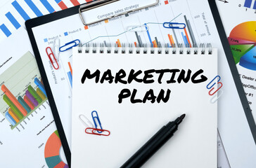 On the table are reports, charts, a notebook with the inscription - MARKETING PLAN