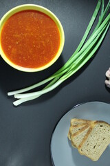 National Russian food red borscht soup in a yellow bowl plate next to lies onion green bread on a black background
