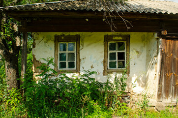 Fototapeta na wymiar Old wooden rustic house plastered with clay and painted with white clay among flowering meadow grasses. House with cracked clay walls and wooden windows.