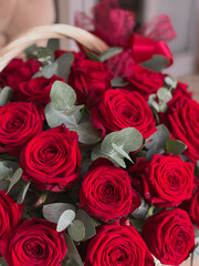 A basket with bright red roses and eucalyptus on a chair in a flower shop. A beautiful bouquet of flowers for the holiday. Background for the postcard