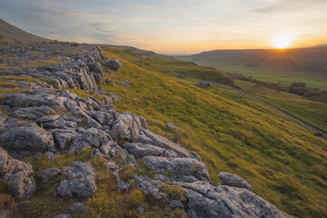 Sunrise or sunset golden light over the beautiful countryside landscape of limestone pavement and moorland at Southerscales in the Yorkshire Dales National Park, UK.