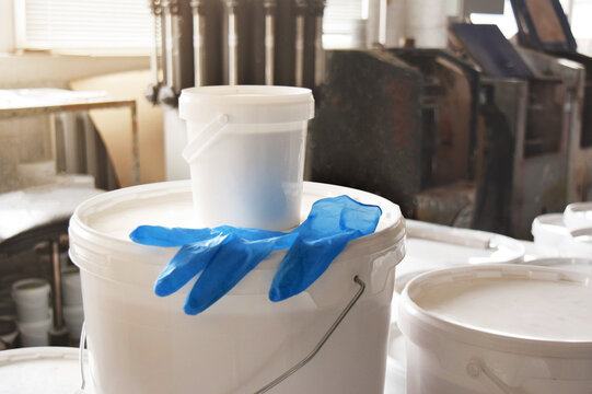 A white paint can sits on a table in a production workshop. Jar along with blue gloves. Production of paints.