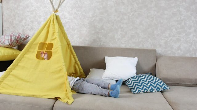 a small child plays at home in a yellow teepee lying on his back swinging his legs