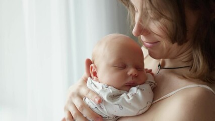 Mother holding a newborn baby in her arms. Young mother is keeping in arms and caressing her newborn baby. - Powered by Adobe
