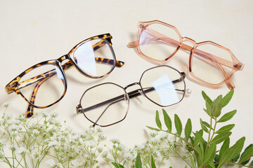 several fashionable glasses and flowers on a beige background copy space top view