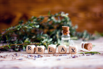 The inscription relax from wooden cubes on a wooden table against the background of bottles with essential oil and spicy herbs. Wellness concept and self-care background