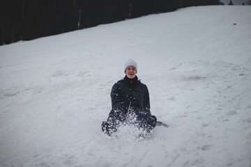 teenager with a happy smile on his face runs down the slopes on a plastic snowboard and rushes down...