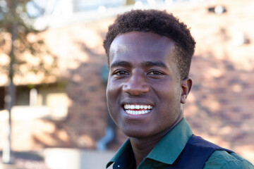 A handsome smiling young black student stands in front of his college