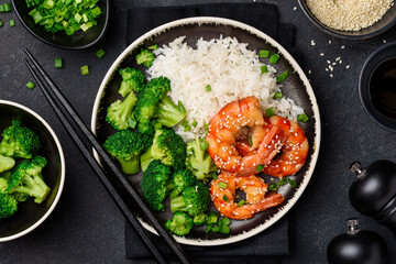 Teriyaki shrimp, rice and broccoli on a black plate. Asian healthy food. Seafood with garnish