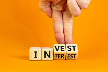 Invest or interest symbol. Businessman turns wooden cubes and changes the word 'invest' to 'interest'. Beautiful orange background, copy space. Business and invest or interest concept.