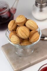 Homemade nut-shaped cookies stuffed with condensed milk in a glass vase on a marble cutting board. Red Sudanese rose tea in a cup and teapot.