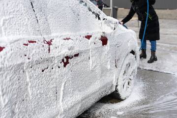 washing car at autowash . Car wash. red machine under the pressure of water at a car wash. car in foam. woman washing car