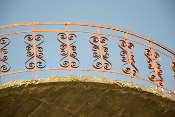 Modern red balcony, red openwork wrought iron fence with heart shapes against blue sky, railings, exterior of a building, unfinished floor