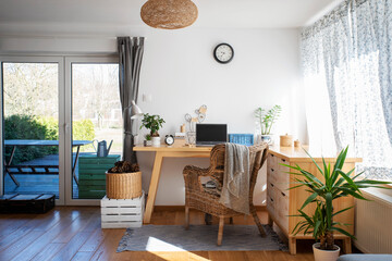Room at home with office desk for work with laptop, plant and clock. Wooden furniture and floor and...
