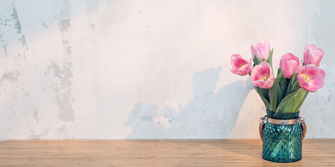 Pink tulips in green vase on wooden table in sunlight from window