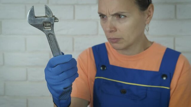 Surprised woman with monkey wrench. The woman looks at the adjustable wrench in bewilderment.