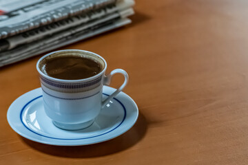 A cup of Turkish coffee and old newspaper on the wooden table.