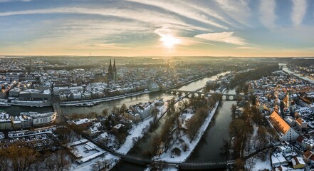 Panorama der Stadt Regensburg in Bayern mit dem Fluss Donau dem Dom und der steinernen Br&uuml;cke im Winter mit Eis und Schnee bei Sonnenuntergang, Deutschland