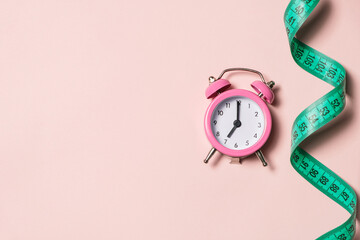 Pink alarm clock with teal measuring tape, top view. Healthy lifestyle, weight loss.