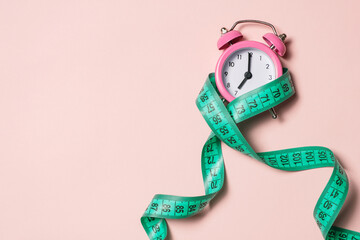 Pink alarm clock with teal measuring tape, top view. Healthy lifestyle, weight loss.