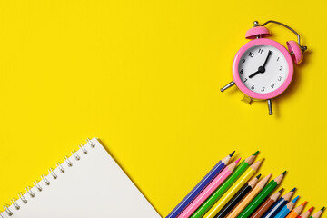 Fototapeta na wymiar Pink alarm clock with office supplies on yellow background.