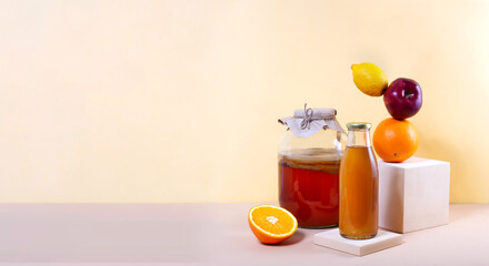 Kombucha tea in glass jar, bottle and balancing fruits for additional flavors on podium on pastel background. Copy space. Orange, apple and lemon balance on modern pedestal. Healthy fermented drink.