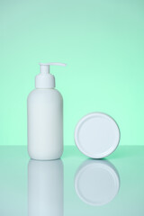 Hand cream in a bottle and jar on a mint background with reflection.